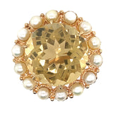 A 9ct yellow gold citrine and pearl brooch with a large round citrine in the centre surrounded by 14 cultured pearls, held against a white background.